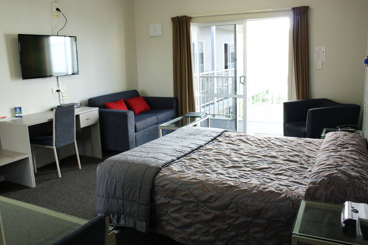 Ein Hotelzimmer mit Bett, Schreibtisch, Stuhl, Fernseher und einem Balkon mit Vorhängen.