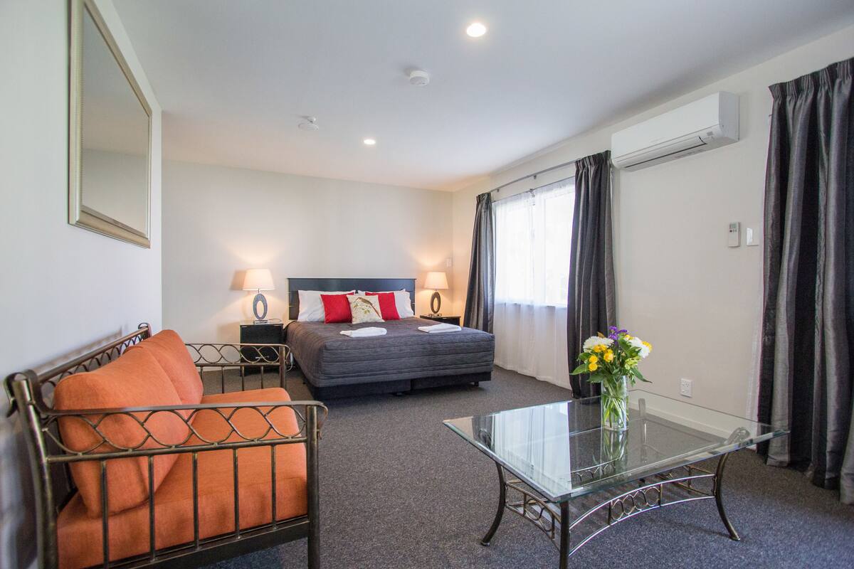 A hotel room with a bed, a glass coffee table, a sofa, and a nightstand with lamps.