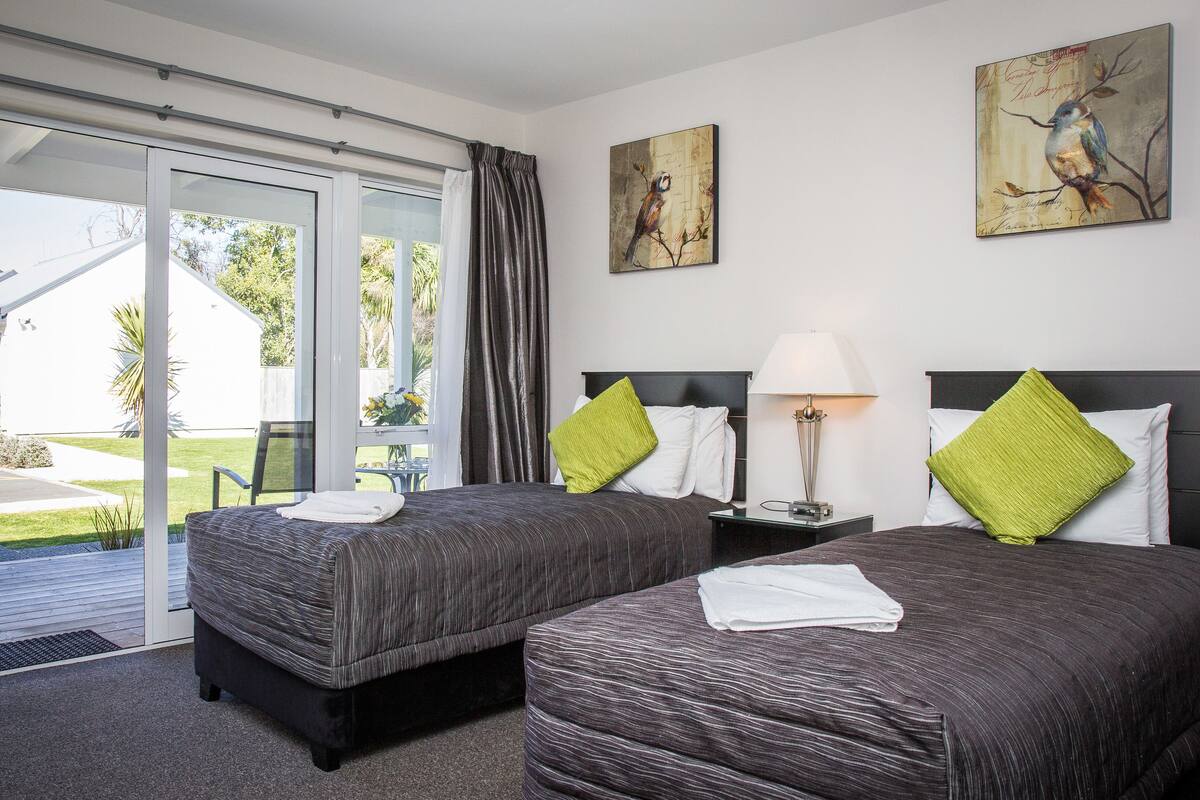 A hotel room with two beds, a sliding glass door to the outside, and artwork on the walls.