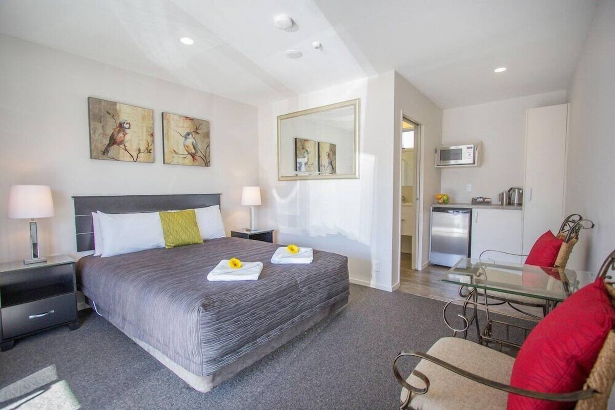 A hotel room with a bed, bedside tables, a desk, a chair, a microwave, and a kitchenette.