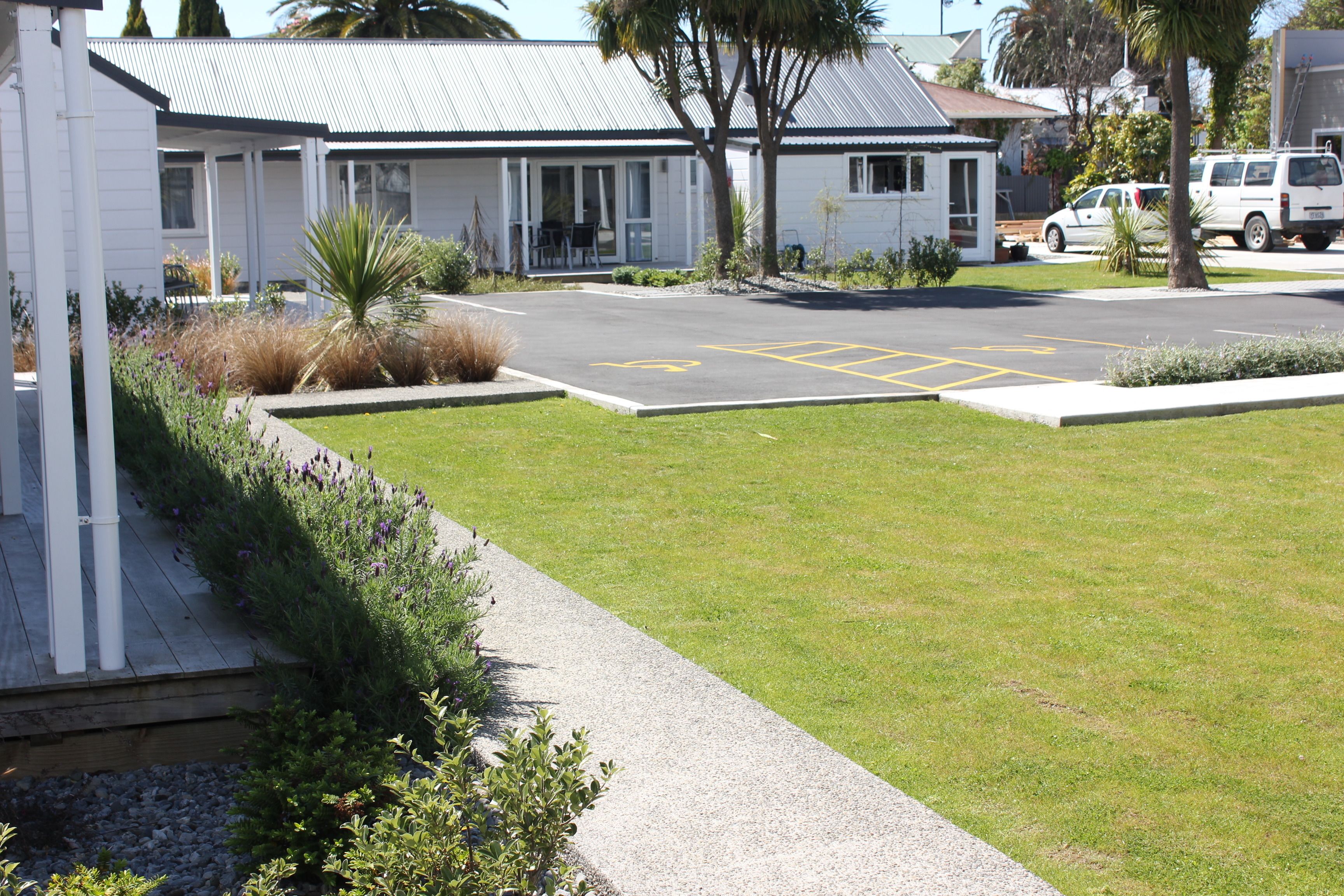 A motel with a covered outdoor seating area, a parking lot, and a small garden.