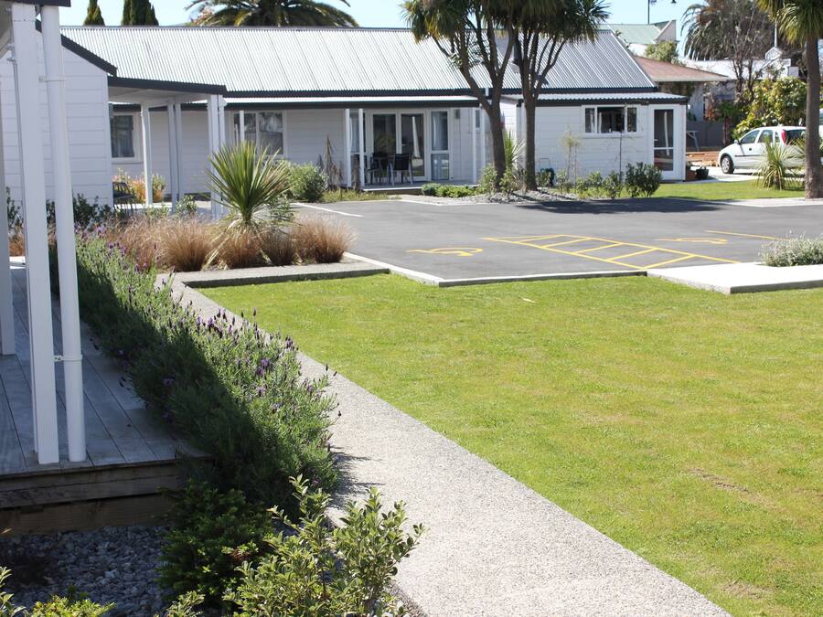A motel with a covered outdoor seating area, a parking lot, and a small garden.