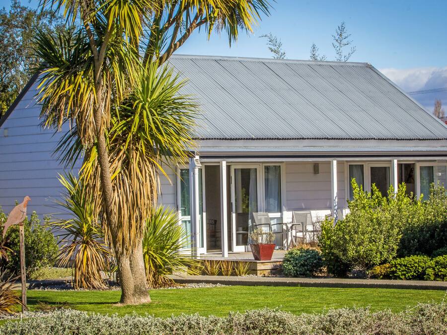 Ein Haus mit überdachter Veranda, Rasen und verschiedenen Pflanzen.