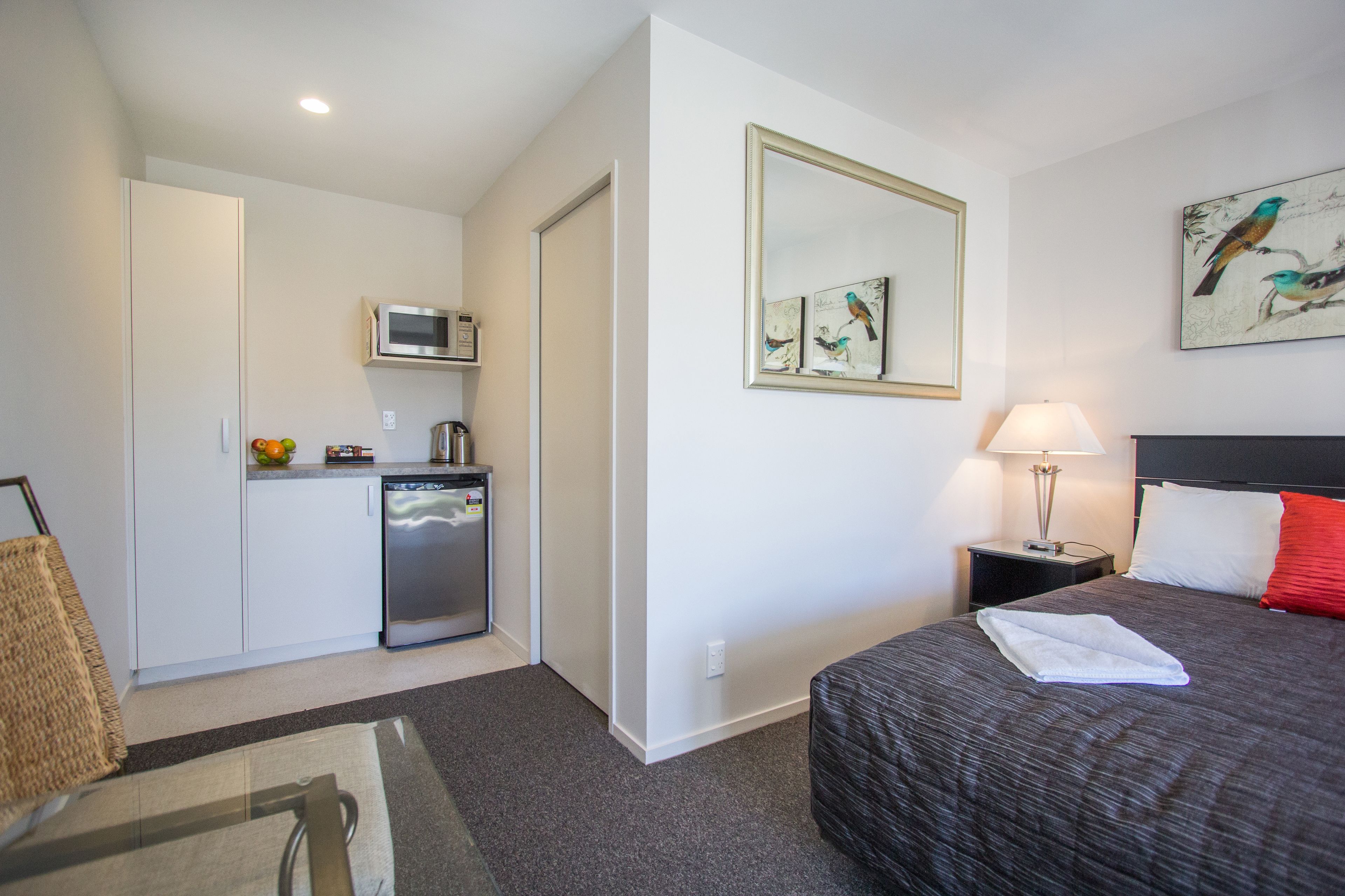 A hotel room with a bed, a nightstand, a lamp, a microwave, a refrigerator, and a painting on the wall.