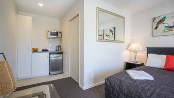 A hotel room with a bed, a nightstand, a lamp, a microwave, a refrigerator, and a painting on the wall.