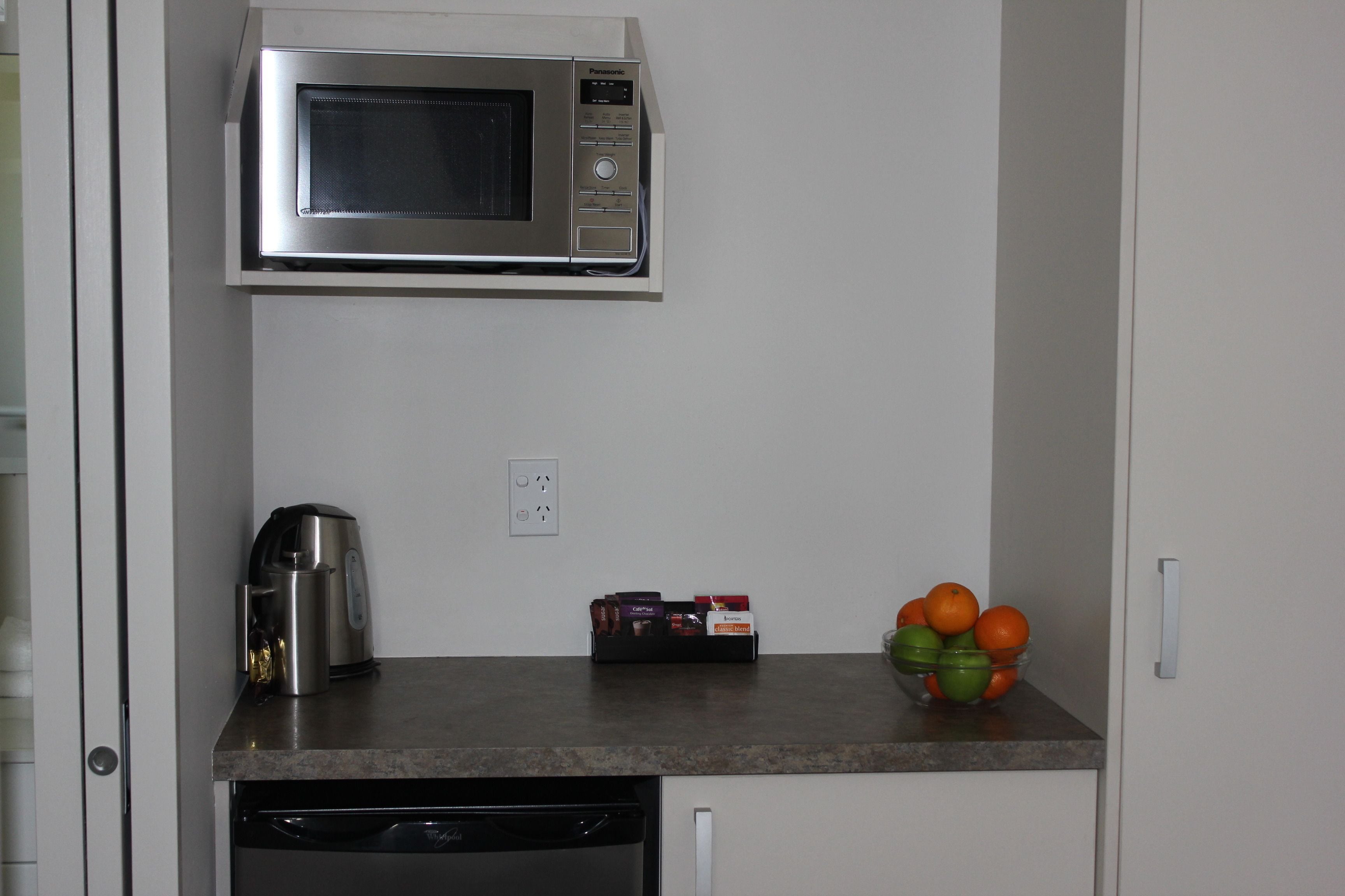 A kitchen with a microwave, coffee maker, and a fruit bowl on the counter.
