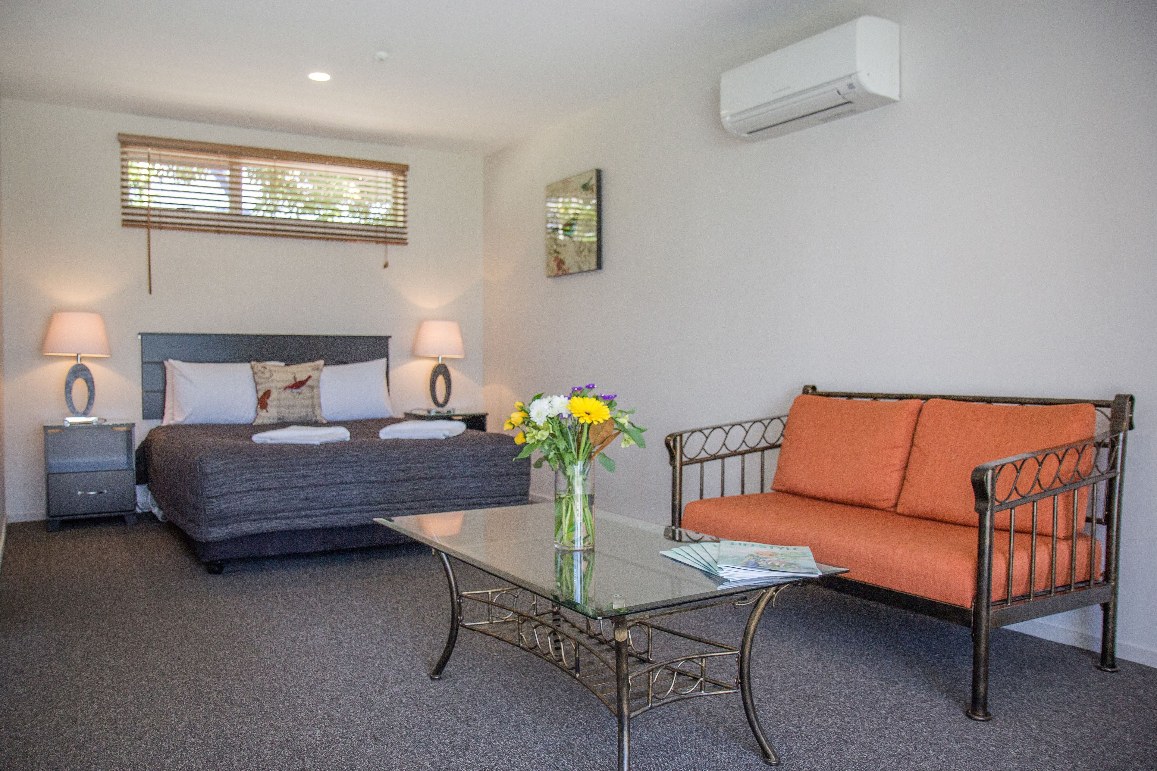 Een slaapkamer met een bed, nachtkastjes, een glazen salontafel, een bank en een airconditioner.