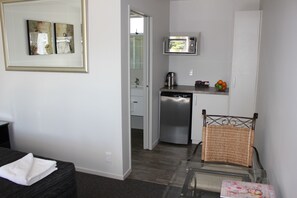 A compact hotel room with a bed, a small kitchenette, and a glass table with a chair. - Greyfriars Motel (Greytown)