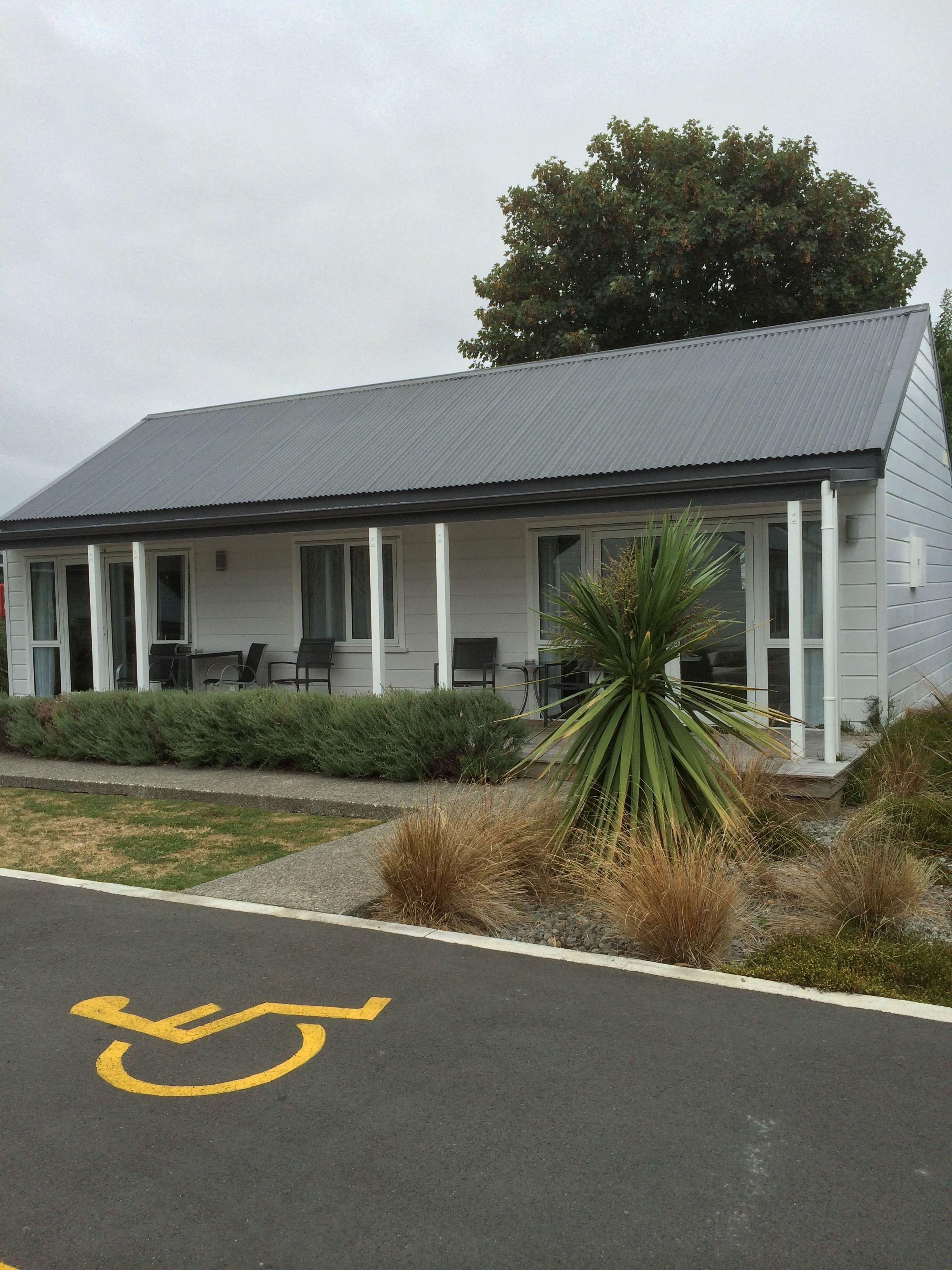 A single-story building with a grey roof and white siding, featuring a covered porch with outdoor seating.