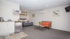 A compact living space with a kitchenette, a sofa, a coffee table, and artwork on the walls. - Greyfriars Motel (Greytown)