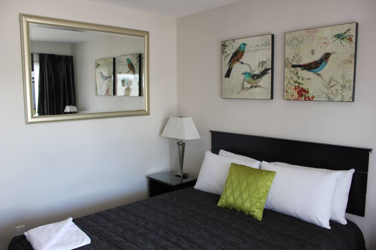 A hotel room with a large bed, a nightstand with a lamp, a mirror, and two wall-mounted bird paintings.