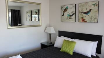 A hotel room with a large bed, a nightstand with a lamp, a mirror, and two wall-mounted bird paintings.