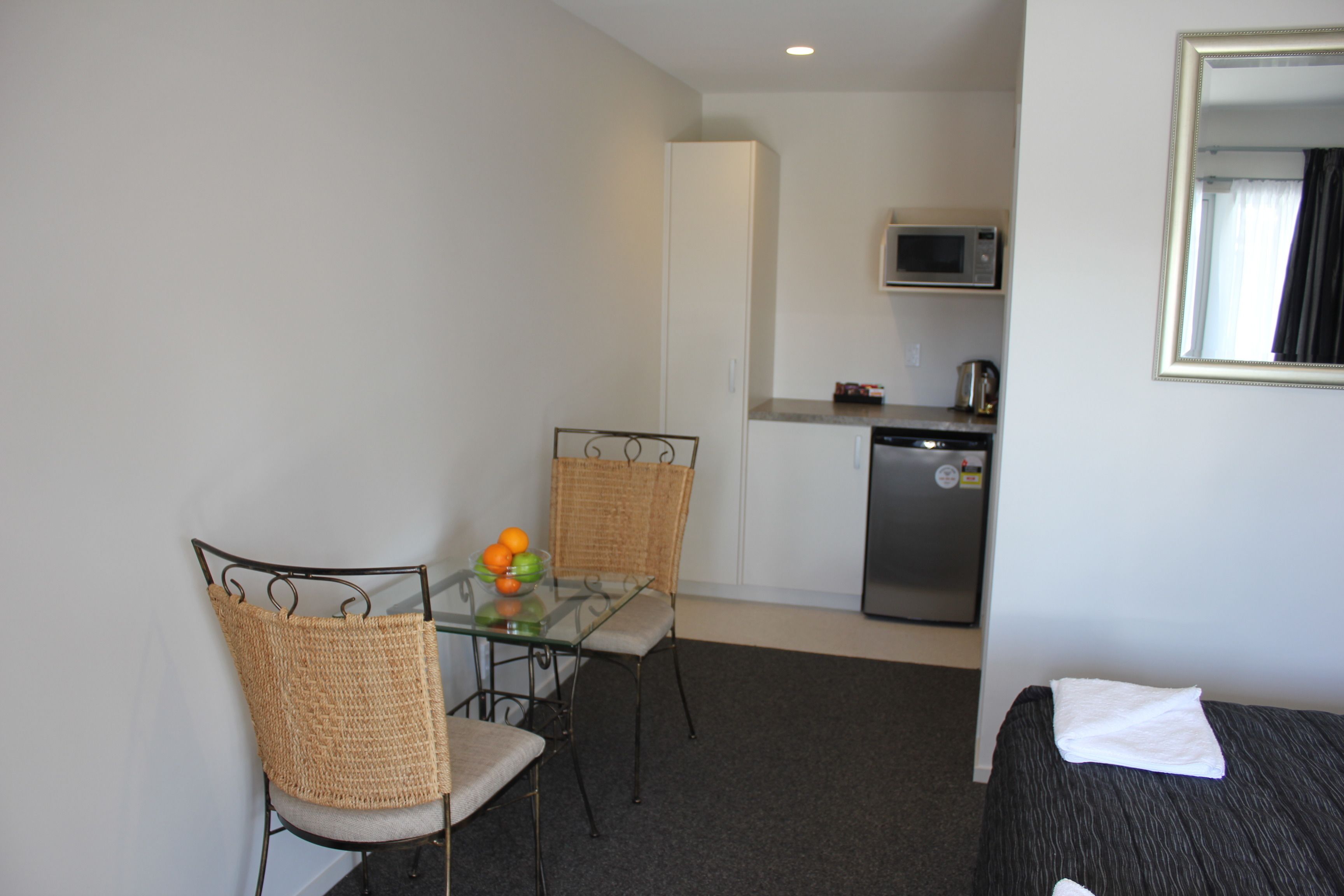 A compact room with a dining table, two chairs, a microwave, and a small kitchenette.
