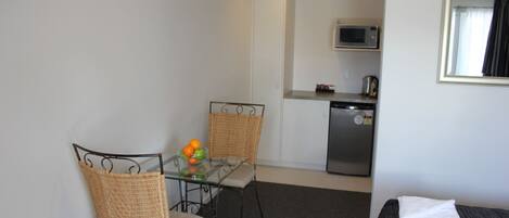A compact room with a dining table, two chairs, a microwave, and a small kitchenette.