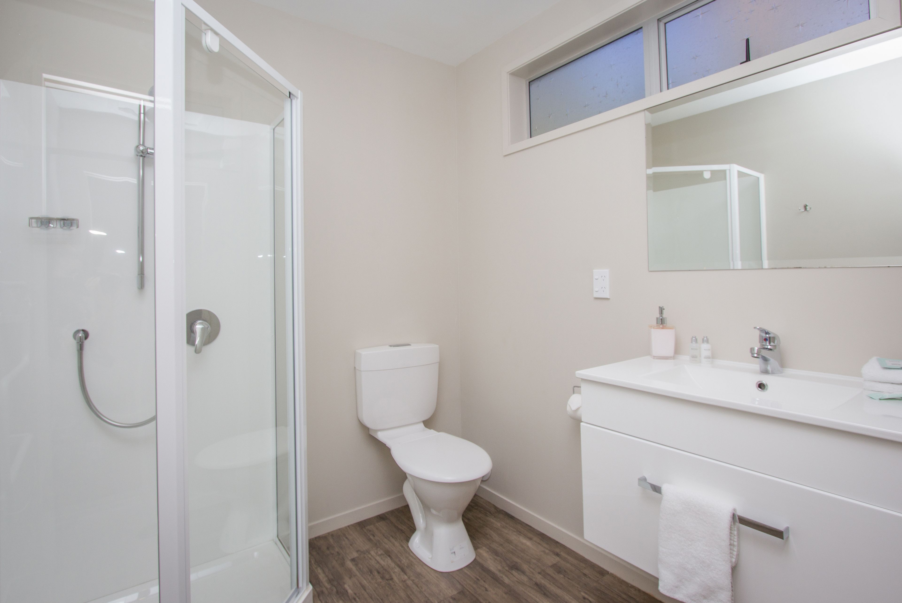 A modern bathroom with a glass shower enclosure, a white toilet, a sink with a mirror above, and a towel rack.