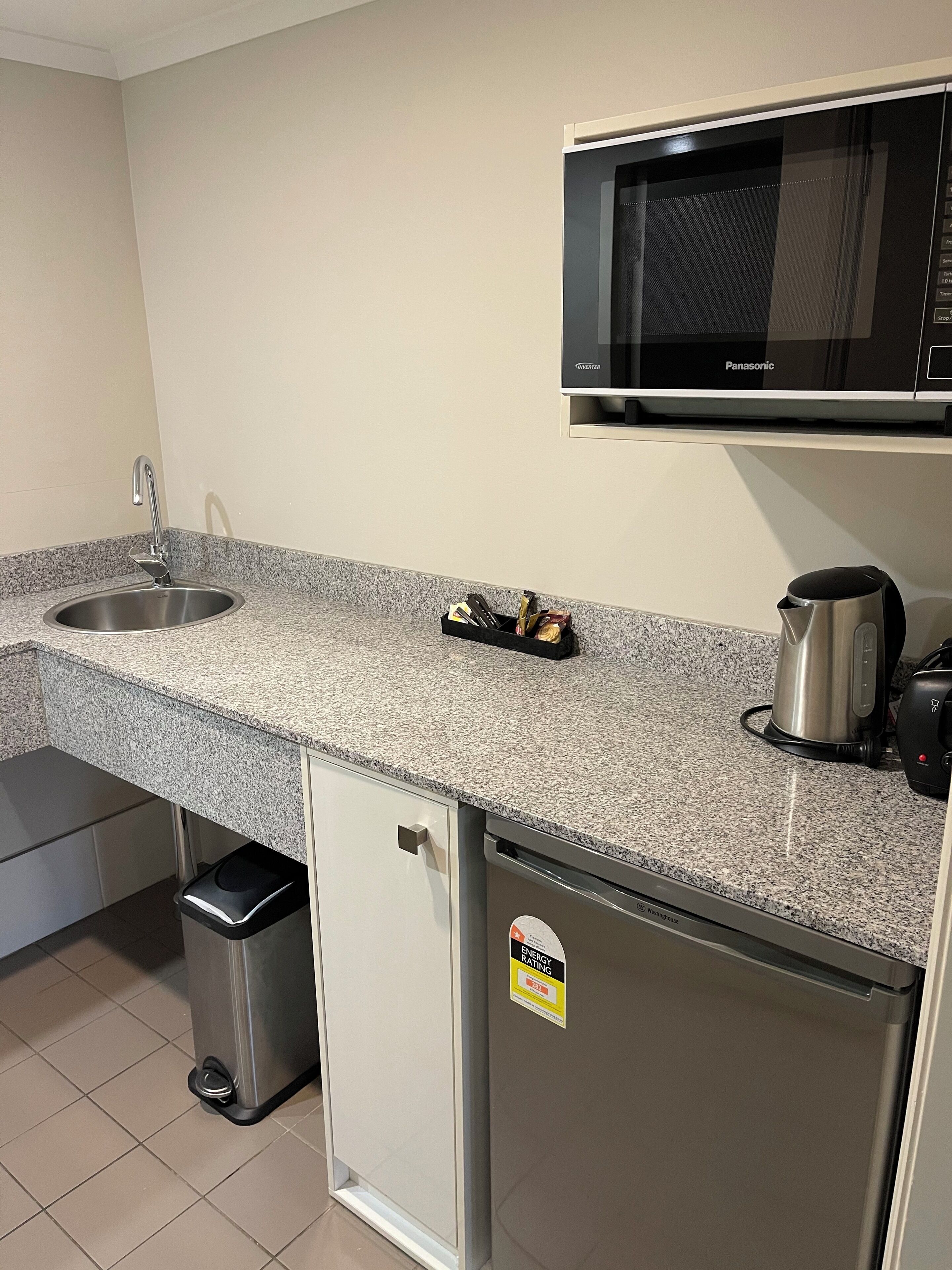 A kitchen with a granite countertop, stainless steel sink, a microwave, a coffee maker, and a refrigerator.