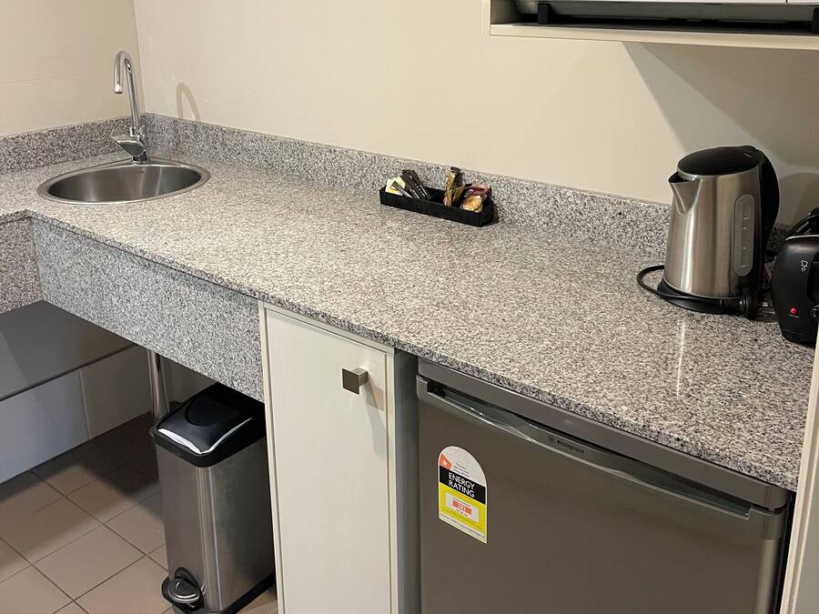 Una cocina con encimera de granito, pileta de acero inoxidable, microondas, cafetera y refrigerador.
