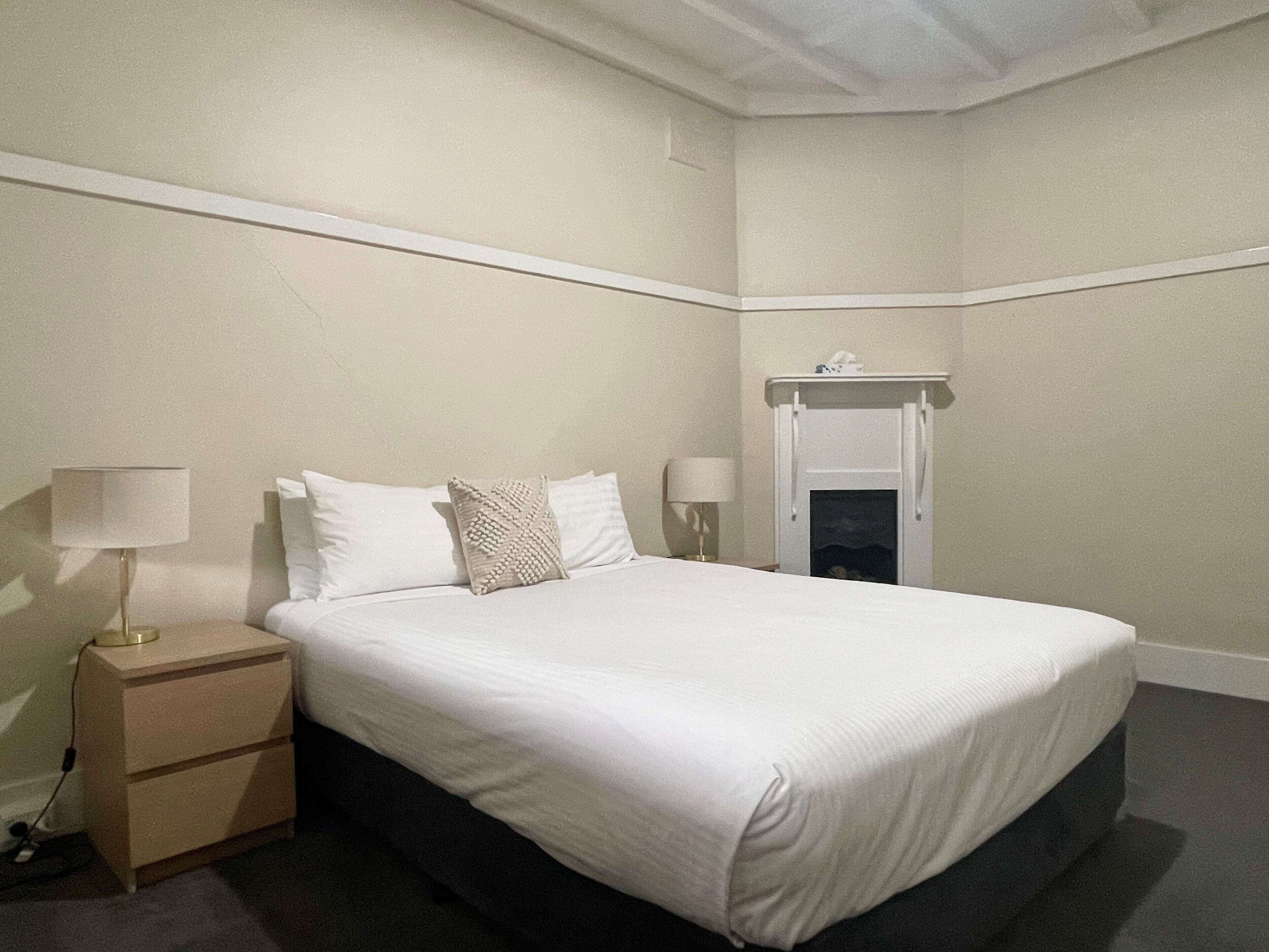 Quarto bem arrumado com cama, abajures, mesa de cabeceira e lareira.