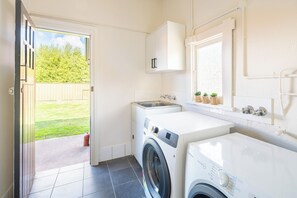 A compact laundry room with a washing machine, dryer, and sink. - Heritage Inn Bathurst (Bathurst)