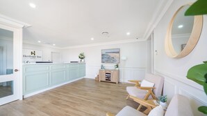 A hotel reception area with a light blue reception desk, a large painting of a beach scene, and a mirror on the wall.