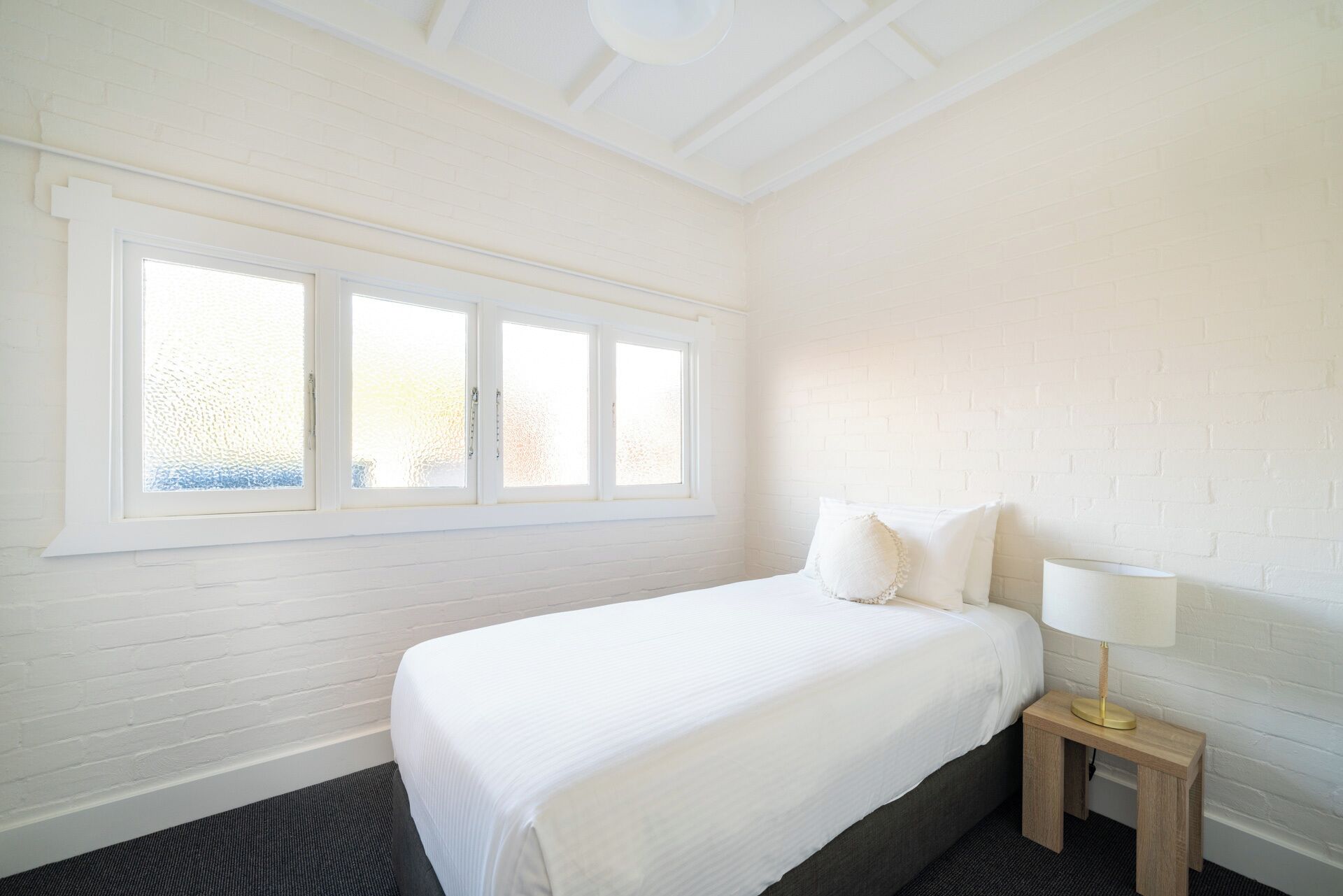A bedroom with a bed, a nightstand with a lamp, and a window with frosted glass.