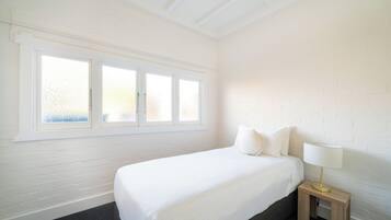 Een slaapkamer met een bed, een nachtkastje met een lamp en een raam met geëtste glas.