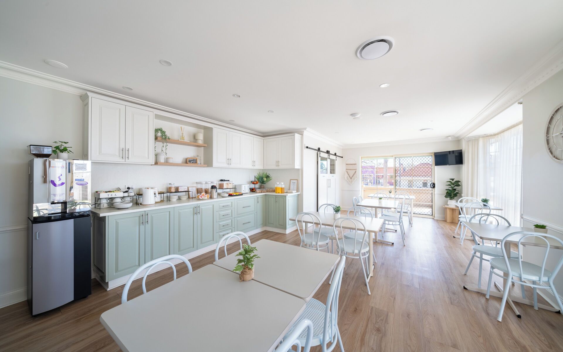 A modern kitchen with white cabinets, a dining area with white chairs, and a large window providing natural light.