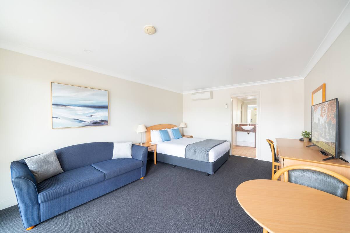 A hotel room with a bed, a sofa, a desk, and a television.