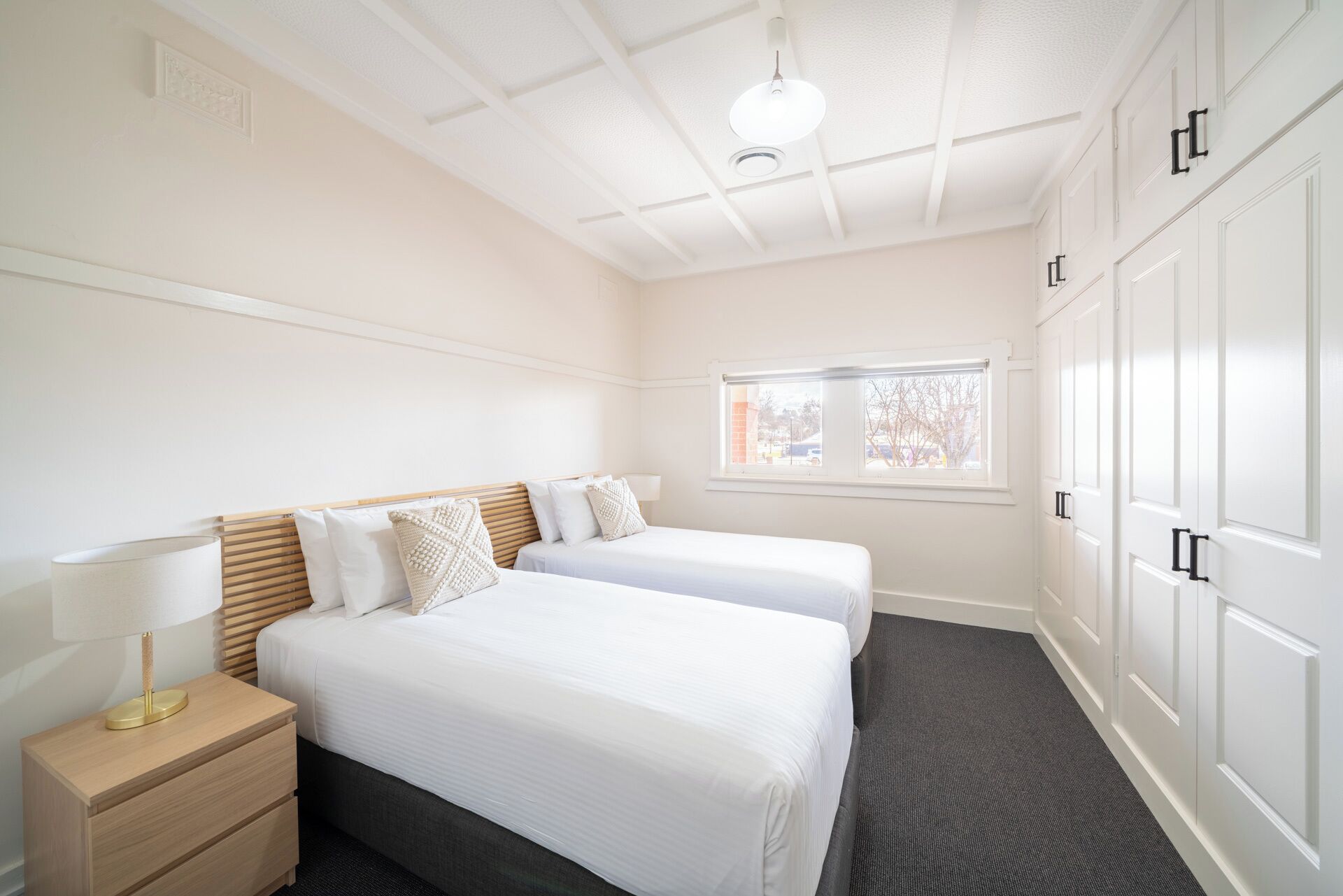A hotel room with two beds, a nightstand, a window, and a wardrobe.
