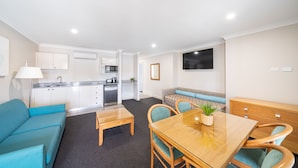A modern apartment with a kitchenette, a dining area, a living room with a sofa, and a TV mounted on the wall.