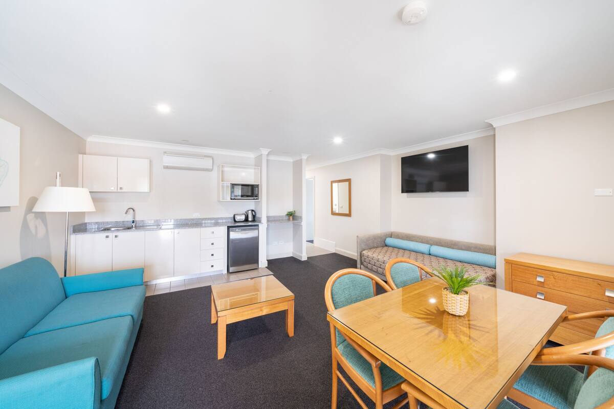 A modern apartment with a kitchenette, a dining area, a living room with a sofa, and a TV mounted on the wall.