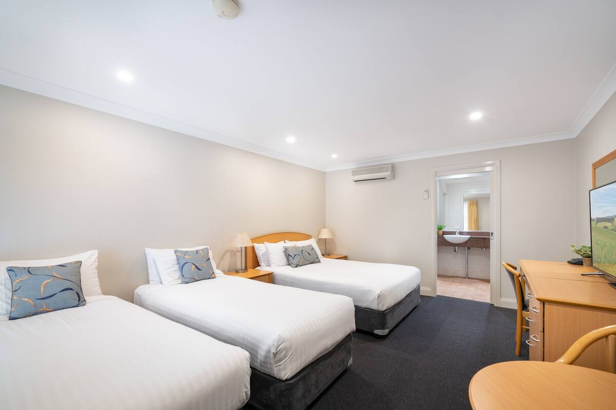 A hotel room with two beds, a desk, and a bathroom visible through an open door.