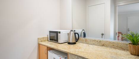 A kitchenette with a microwave, kettle, and a small refrigerator.
