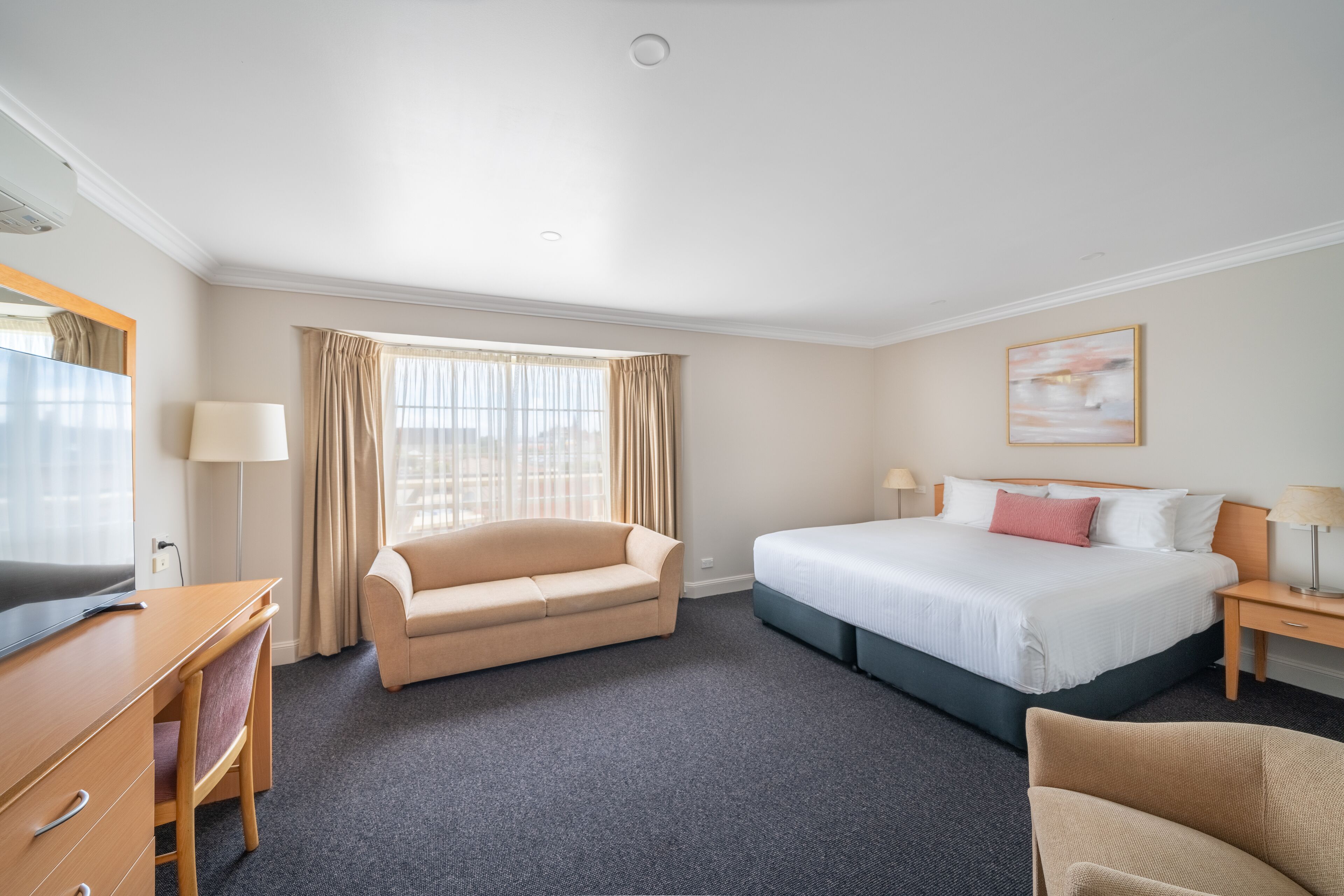 A hotel room with a bed, a sofa, a desk, and a TV.