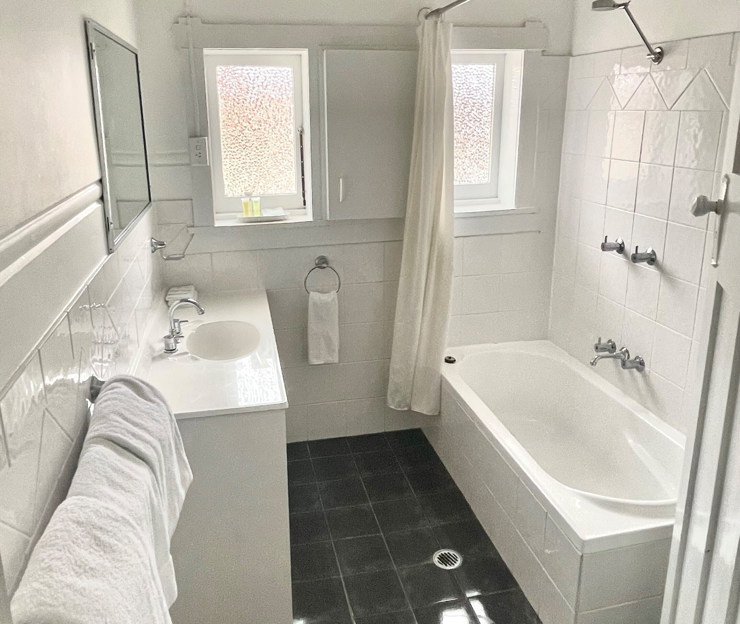 A bathroom with a bathtub, a sink, a mirror, and a window.