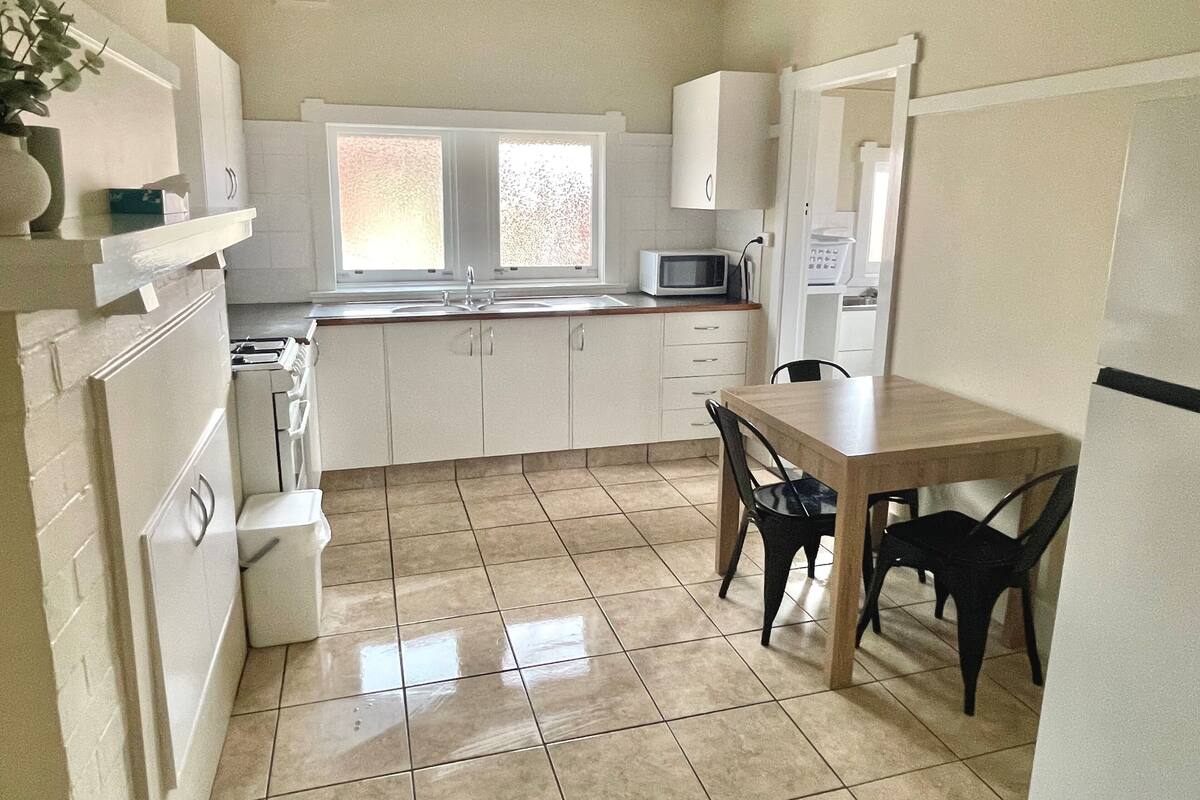 A compact kitchen with white cabinets, a microwave, a sink, and a dining table with chairs.