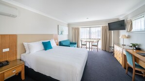 A hotel room with a large bed, a desk with a chair, a TV, and a window with curtains.