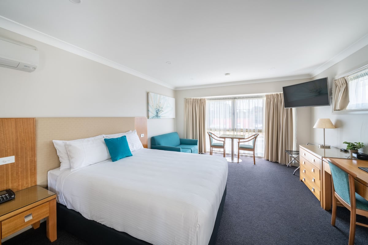A hotel room with a large bed, a desk with a chair, a TV, and a window with curtains.