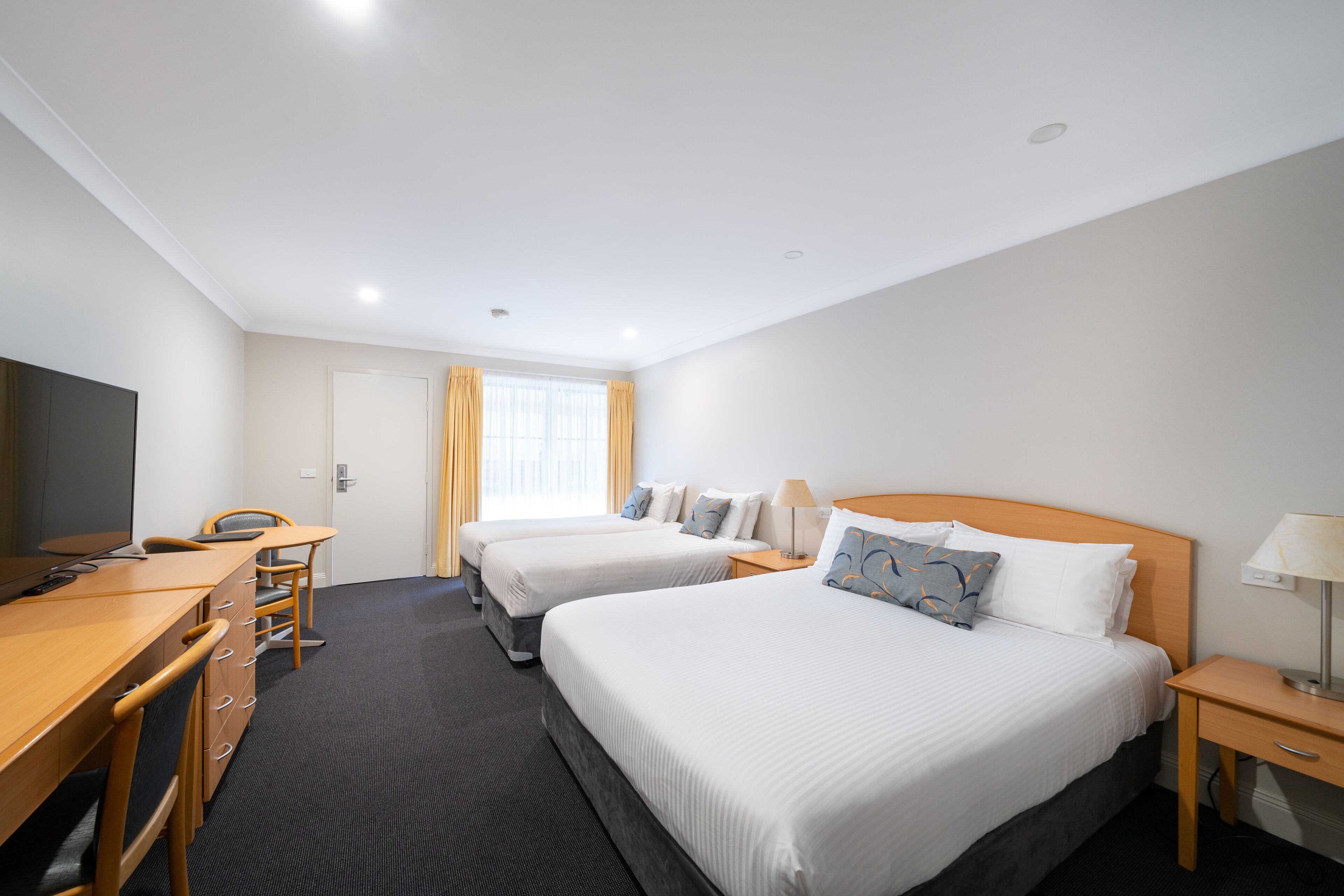 A hotel room with two beds, a desk, a chair, a TV, and a window with curtains.