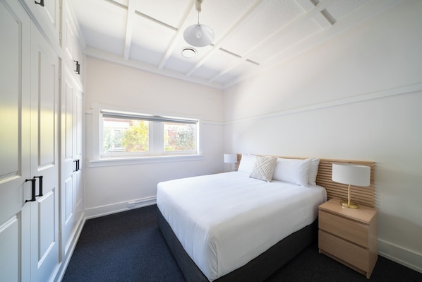 A hotel room with a large bed, a bedside table with a lamp, a window, and a ceiling with recessed lighting.