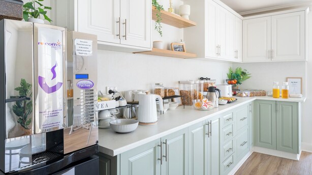 A modern kitchen with white cabinets, a coffee machine, and various breakfast items on the counter.