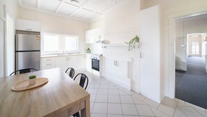 A modern kitchen with white cabinetry, a stainless steel refrigerator, a dining table with chairs, and a tiled floor.