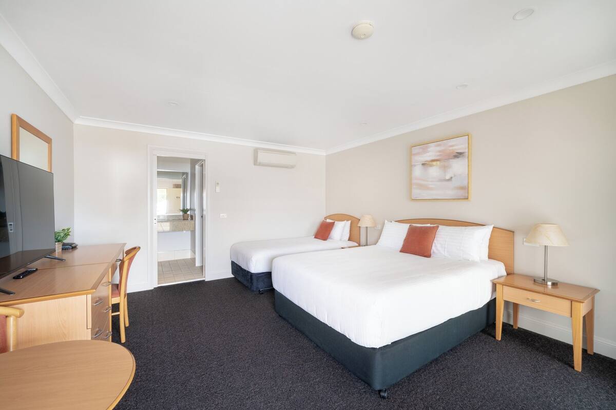 A hotel room with two beds, a desk, a chair, a TV, and a painting on the wall.
