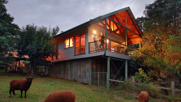 Ein rustikales Scheunenhaus mit Balkon, umgeben von einer Wiese mit Schafen.