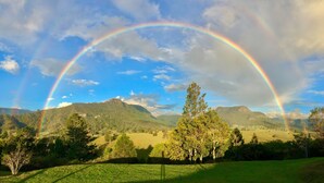 Eine Landschaft mit zwei Regenbögen über hügeligem Gelände mit Bäumen und offenen Feldern.