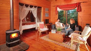Ein gemütliches Blockhaus-Interieur mit Kaminofen, Korbmöbeln und einem großen Fenster mit Blick ins Freie.