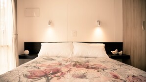 A bed with a floral bedspread, two bedside tables with decorative items, and wall-mounted lights. - Mt Buffalo Caravan Park (Porepunkah)