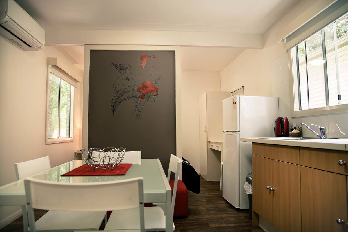 A compact kitchen with a dining area, featuring a refrigerator, a sink, and a window.