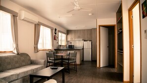 A compact living space with a sofa, dining table, and chairs, a kitchenette with a microwave and refrigerator, and a ceiling fan. - Mt Buffalo Caravan Park (Porepunkah)
