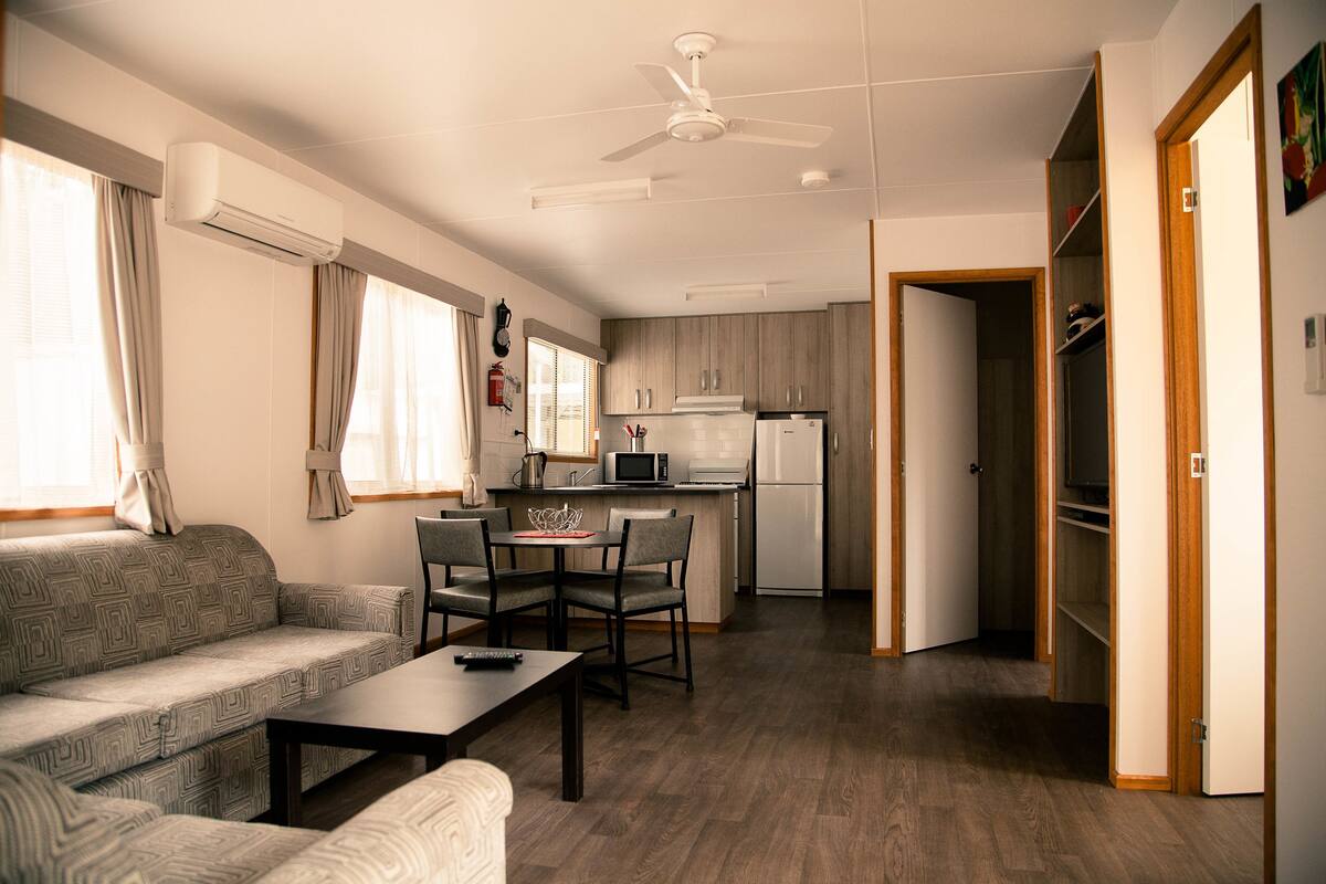 A compact living space with a sofa, dining table, and chairs, a kitchenette with a microwave and refrigerator, and a ceiling fan.